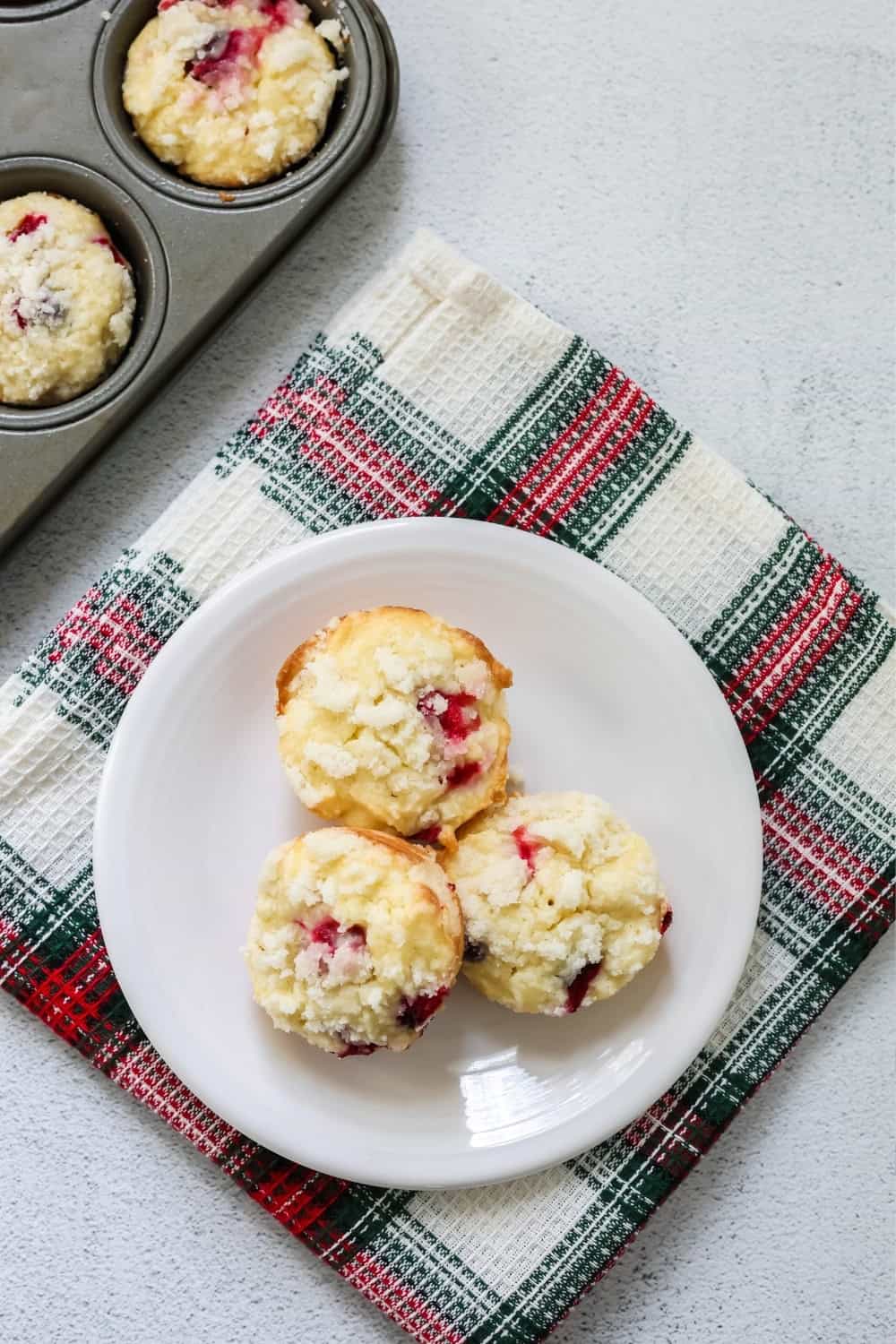 overhead view of cranberry streusel muffins on a white plate, with the muffin tin of remaining muffins in the background.