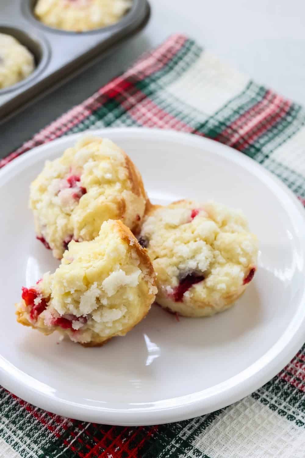 Three cranberry cream cheese muffins on a white plate, one of which has a bite taken out of it.