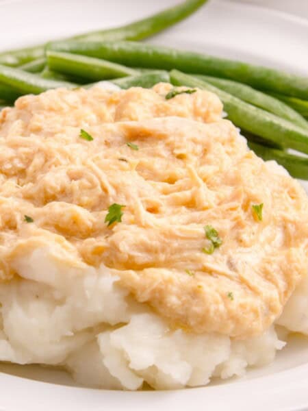 Crock Pot chicken and gravy served over mashed potatoes on a white plate.