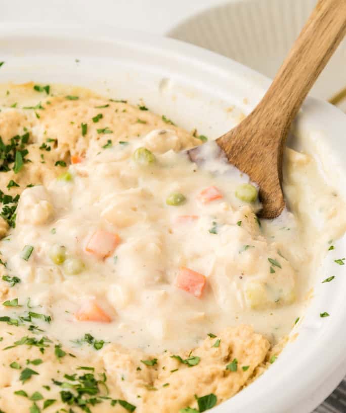 Crock Pot chicken and Bisquick dumplings, freshly cooked, with a wooden serving spoon scooping some out.