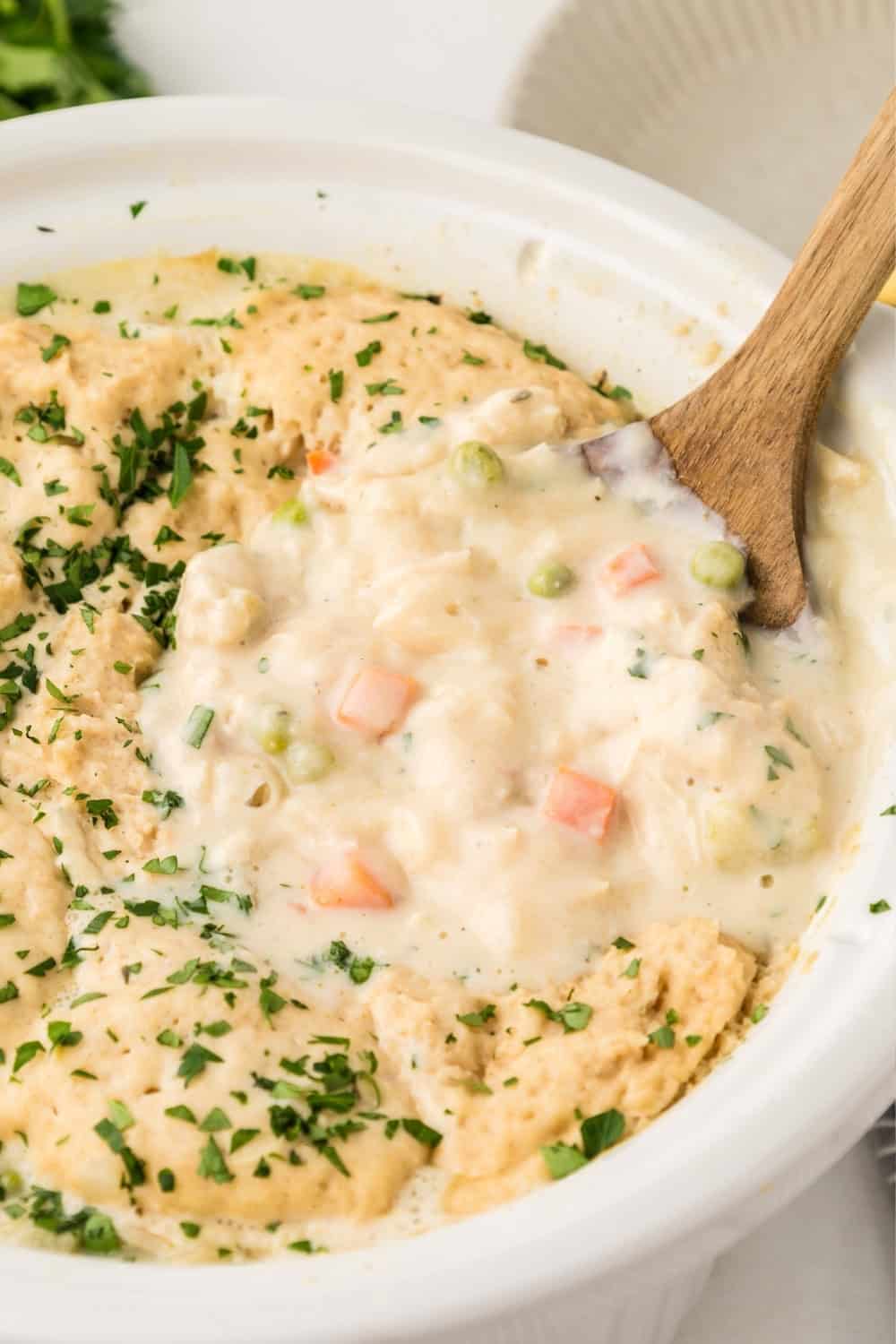 a wooden serving spoon scoops out chicken and bisquick dumplings from a slow cooker.