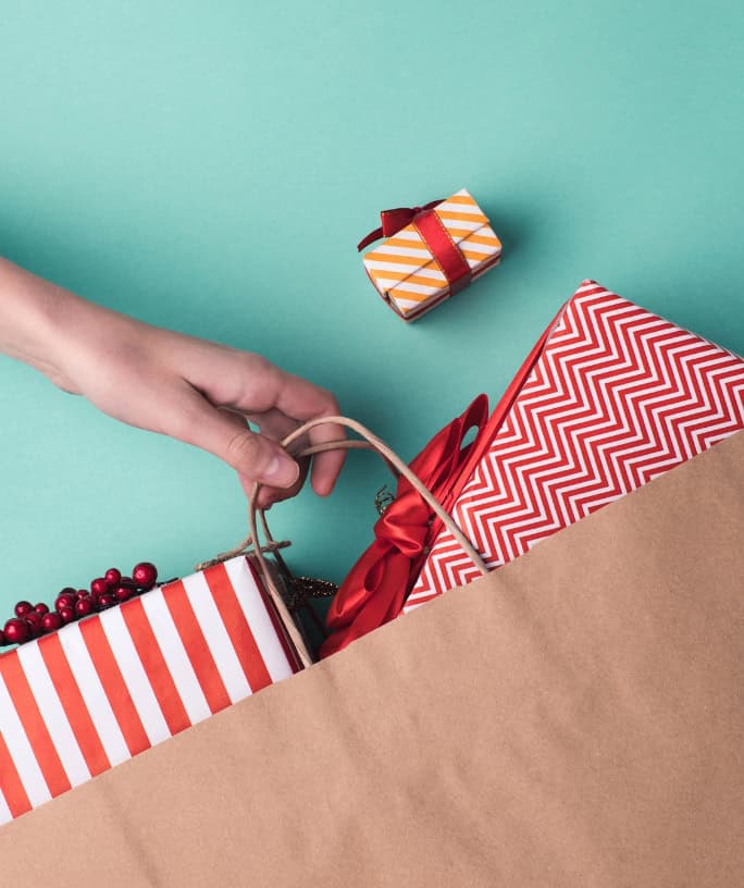 a hand holds a paper bag filled with red and white wrapped gifts for tweens.