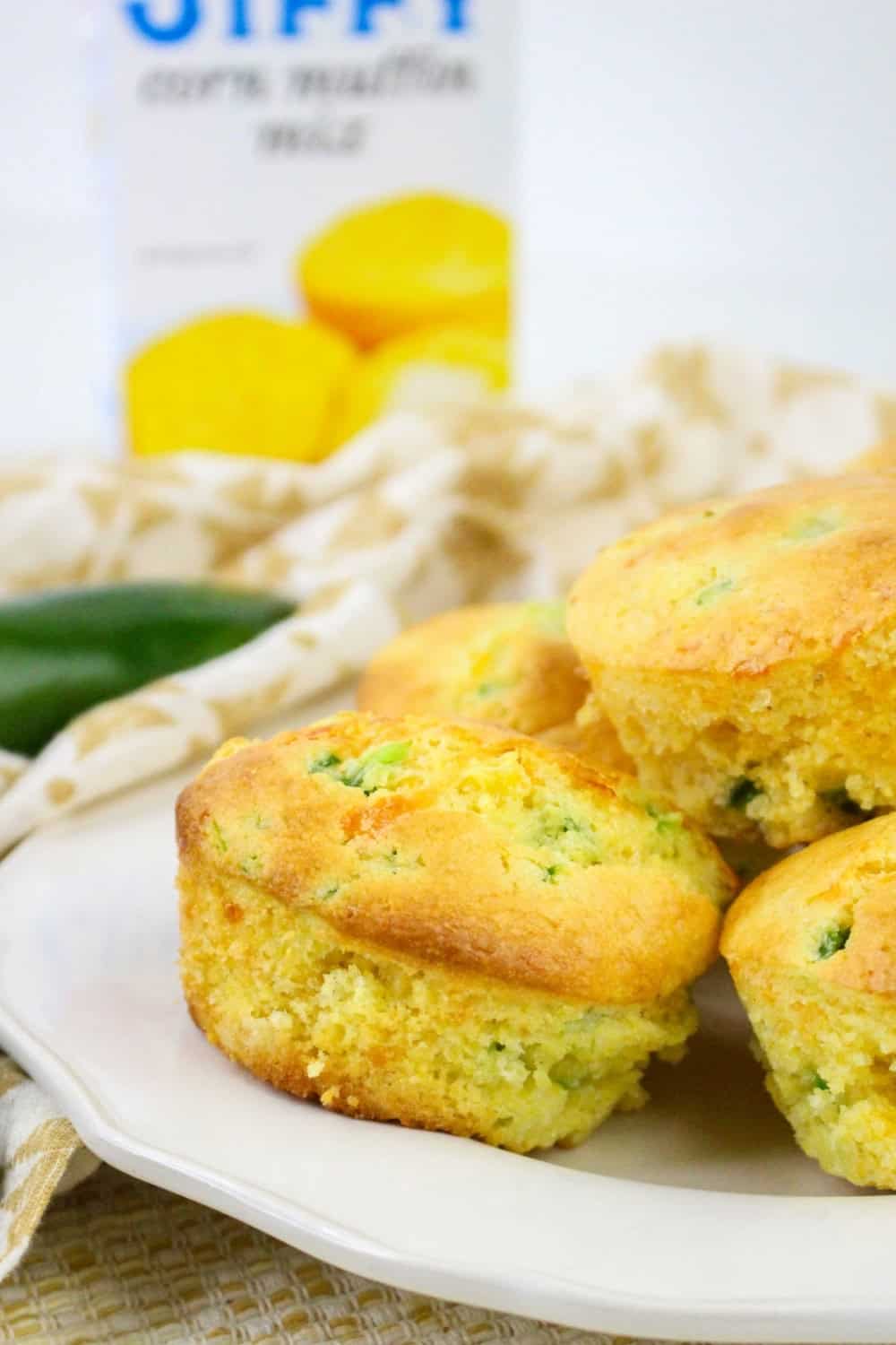a few jalapeno corn muffins with cheese are served on a white plate, with a box of Jiffy mix in the background.