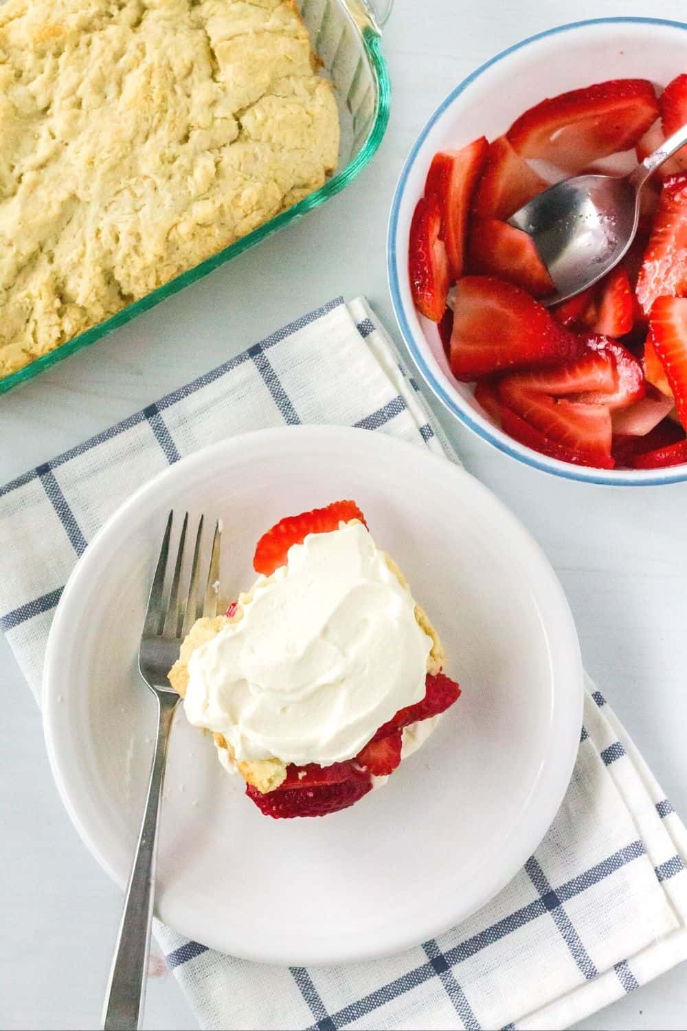 overhead view of strawberry shortcake made from scratch, served on a white plate, with berries and additional shortcake in the background.