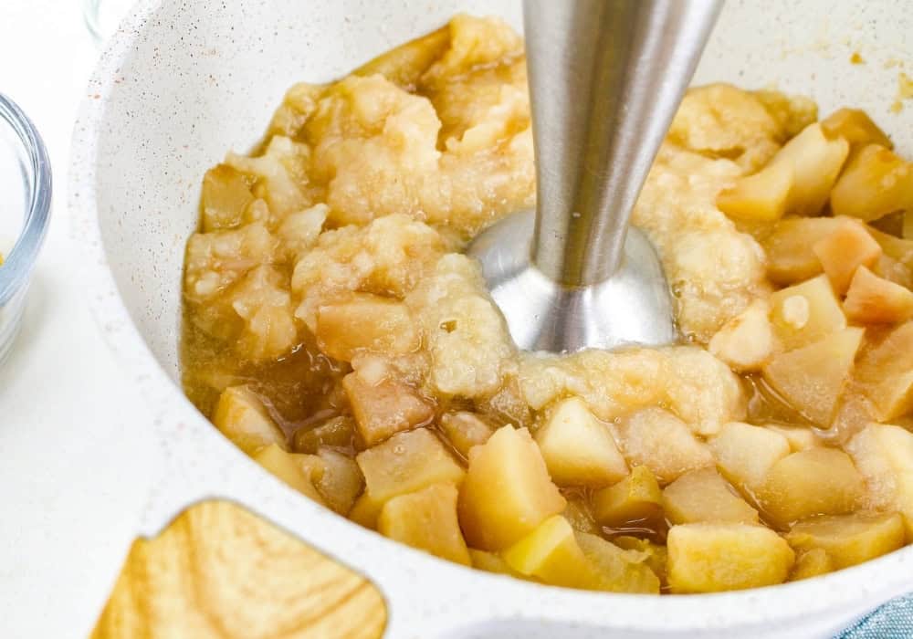an immersion blender is blending the cooked pears and apples to create apple pear sauce.