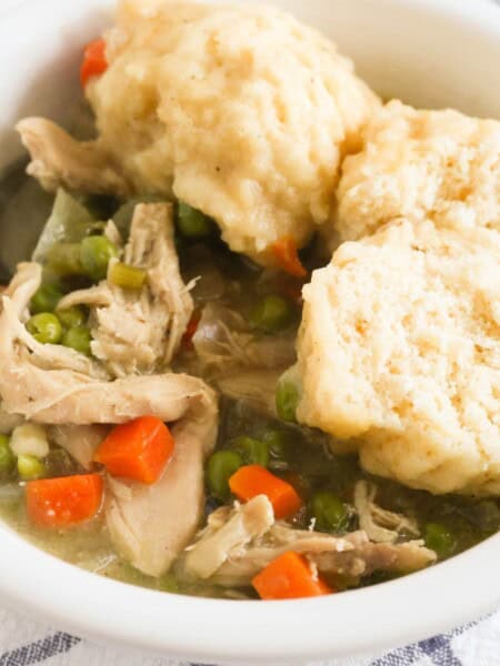 close-up view of a white bowl of homemade chicken and cornmeal dumplings. One dumpling is cut in half to show the fluffy interior.