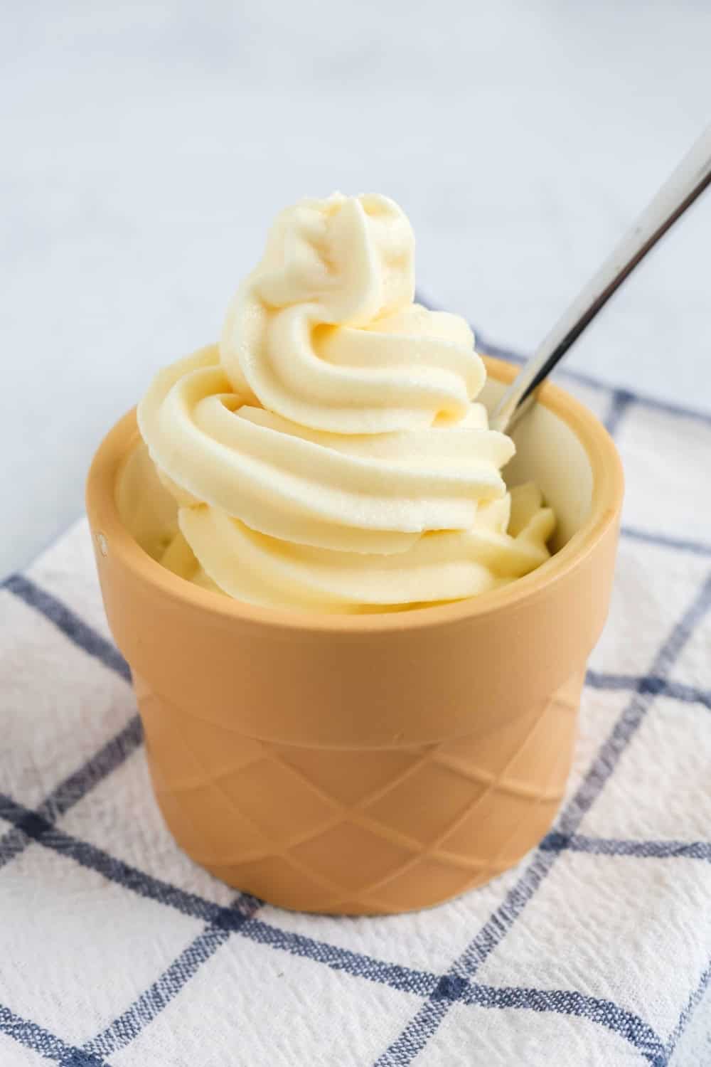 side view of a cup of Ninja Swirl by Creami vanilla soft serve with a spoon in it.
