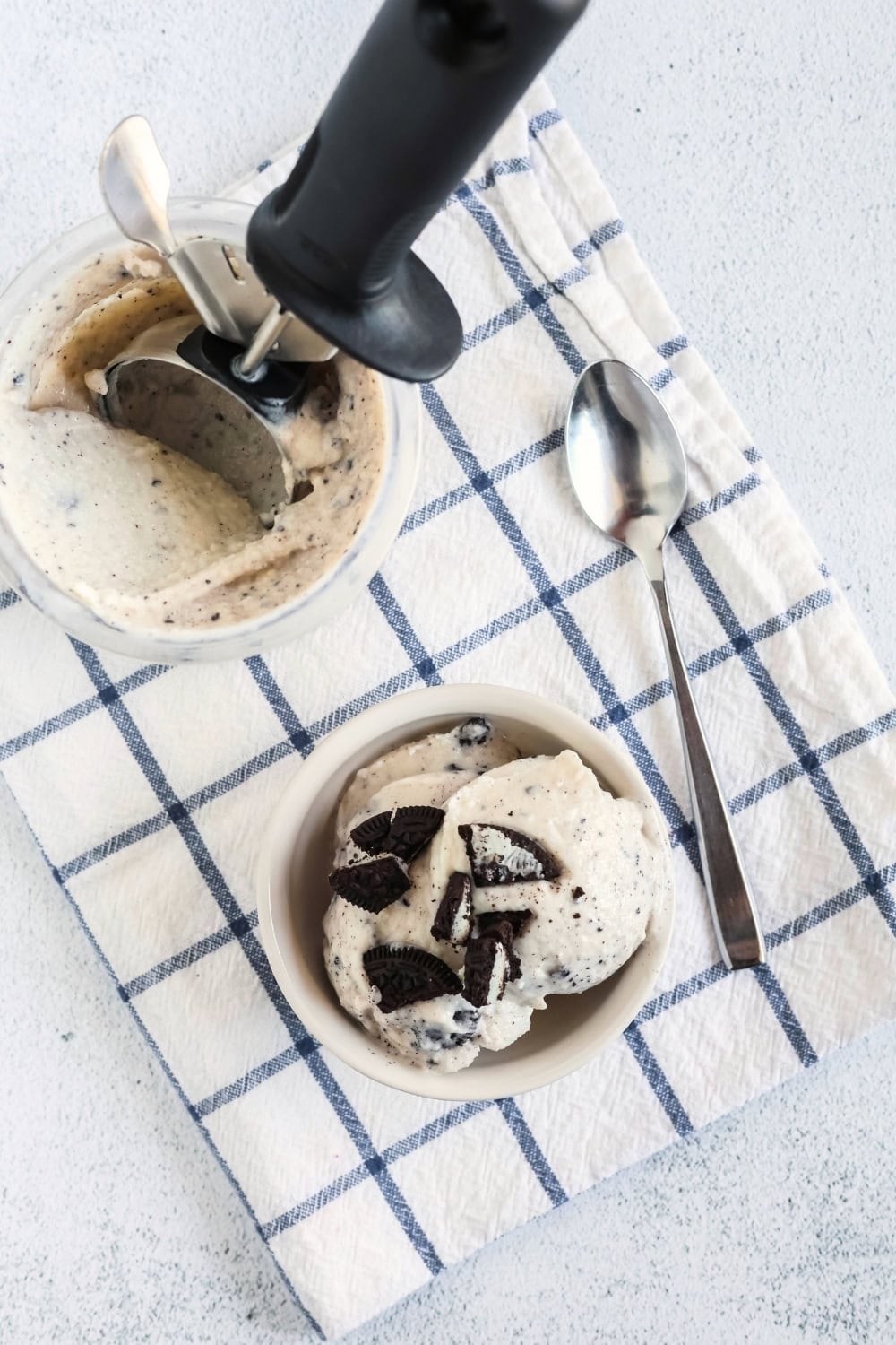 overhead view of a pint of Ninja Creami cookies and cream frozen yogurt. Next to it is a dessert bowl serving scoops of the Oreo frozen yogurt. A spoon is next to the bowl.