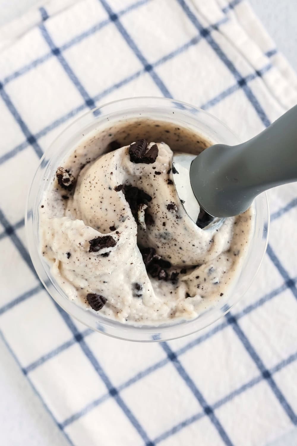 Overhead view of a pint of cookies and cream frozen yogurt with an ice cream scoop in it.