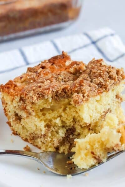 a slice of pear coffee cake is served on a white plate. A fork has cut out a bite of cake and is resting on the plate.