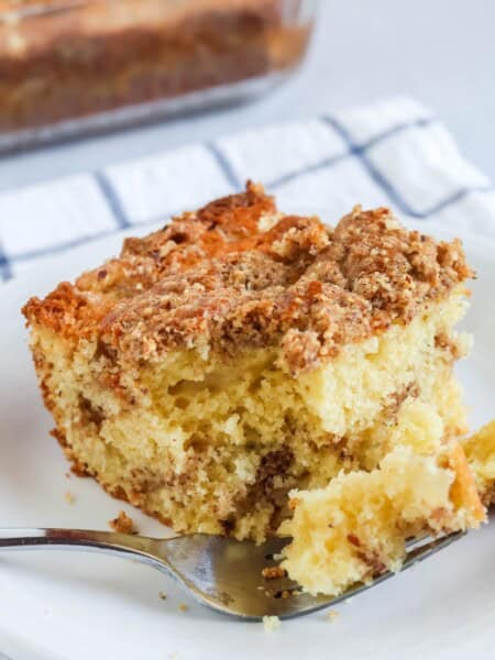a slice of pear coffee cake is served on a white plate. A fork has cut out a bite of cake and is resting on the plate.