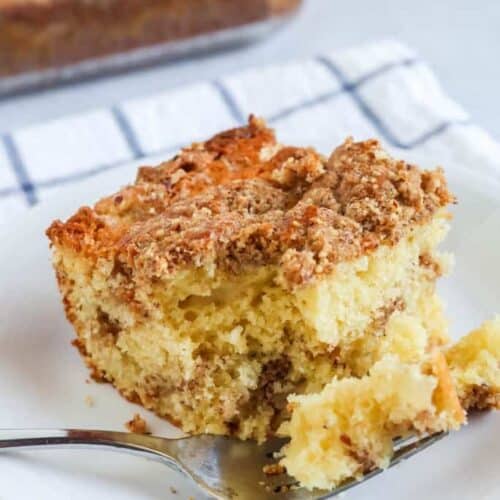 a slice of pear coffee cake is served on a white plate. A fork has cut out a bite of cake and is resting on the plate.