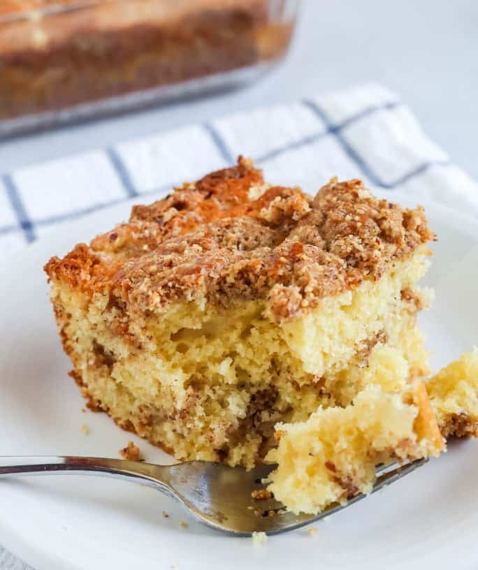 a slice of pear coffee cake is served on a white plate. A fork has cut out a bite of cake and is resting on the plate.