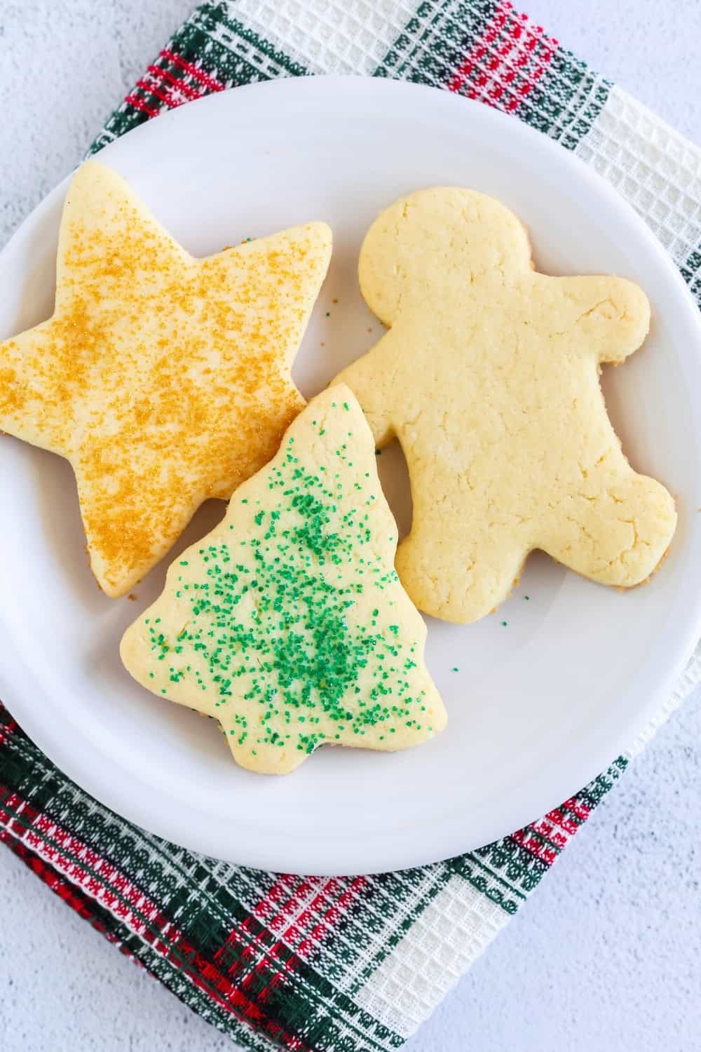 a white plate serves three Christmas sugar cookies made with cake mix. Two are decorated with sanding sugar.