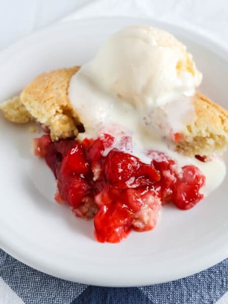 Bisquick strawberry cobbler served on a white plate and topped with a scoop of vanilla ice cream. The cobbler is warm and the ice cream is starting to melt.