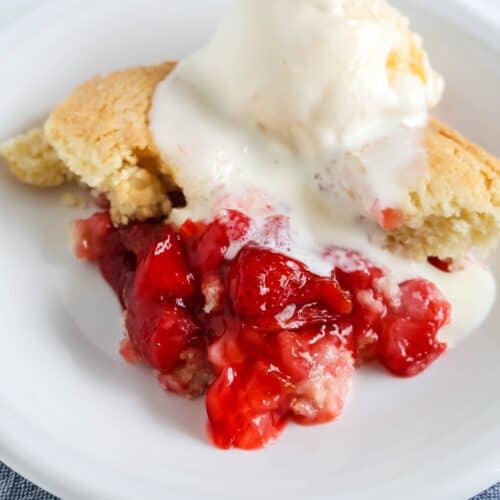 Bisquick strawberry cobbler served on a white plate and topped with a scoop of vanilla ice cream. The cobbler is warm and the ice cream is starting to melt.