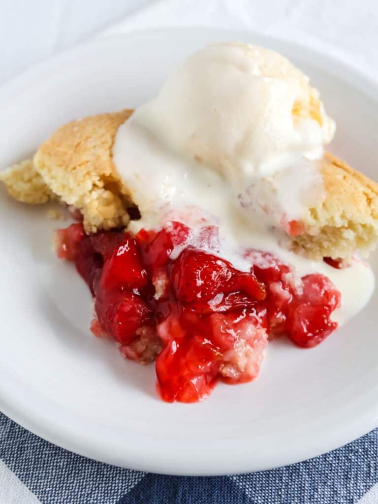 Bisquick strawberry cobbler served on a white plate and topped with a scoop of vanilla ice cream. The cobbler is warm and the ice cream is starting to melt.