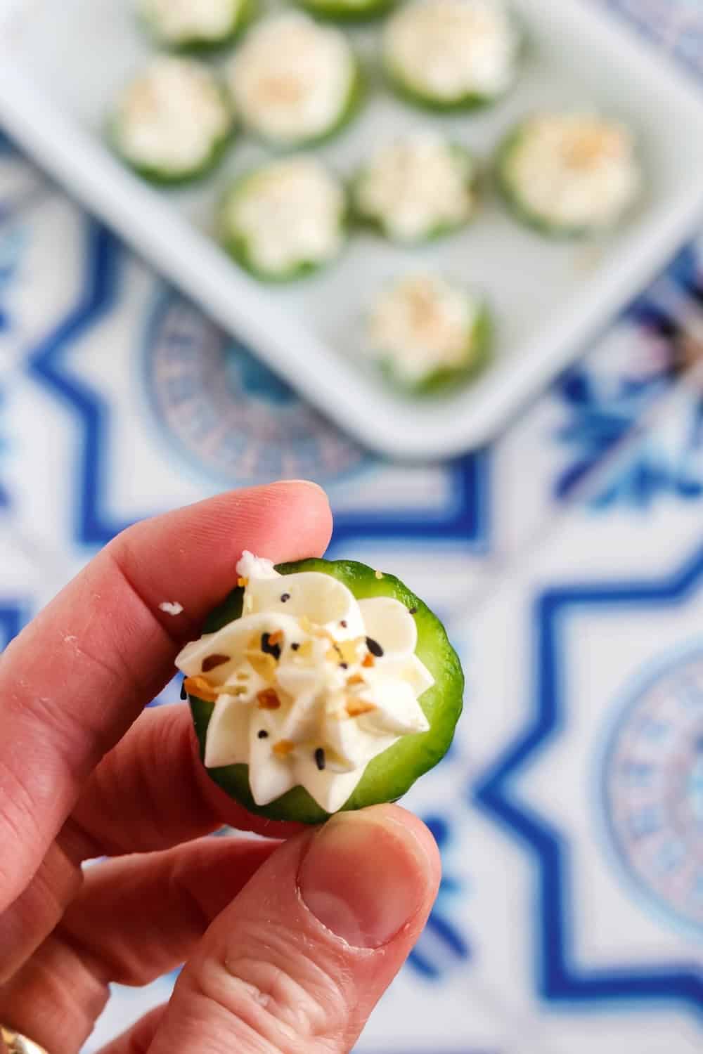 a hand holds a cucumber cream cheese bite sprinkled with everything bagel seasoning.