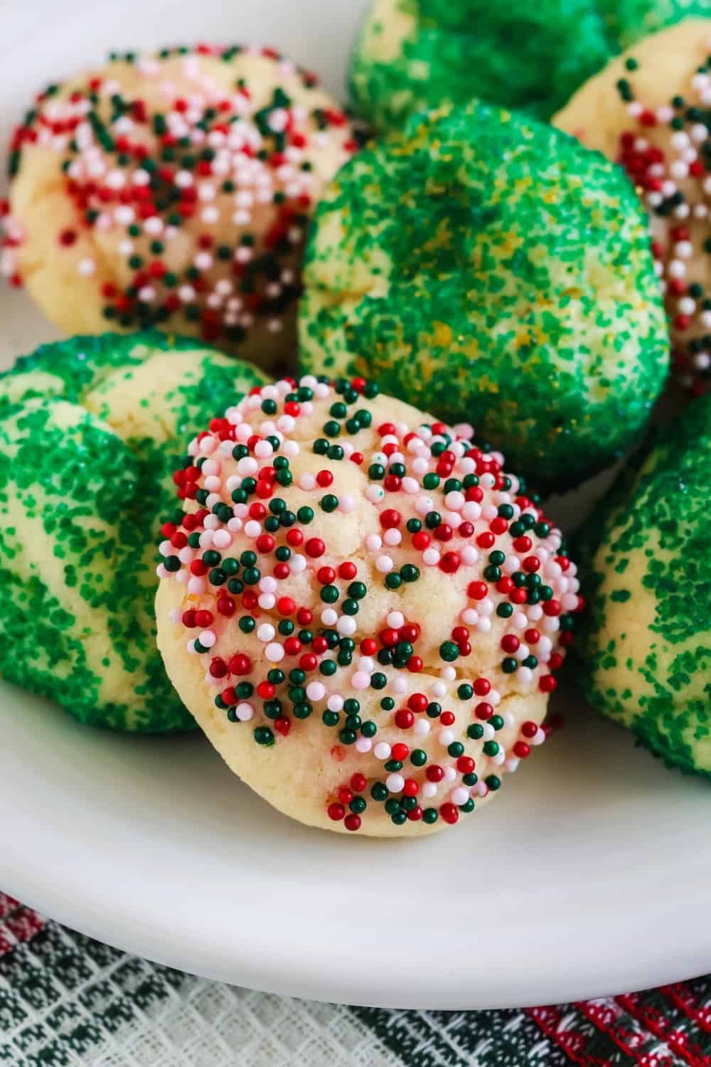 close-up view of freshly baked sprinkle-covered holiday cake mix cookies on a white plate.