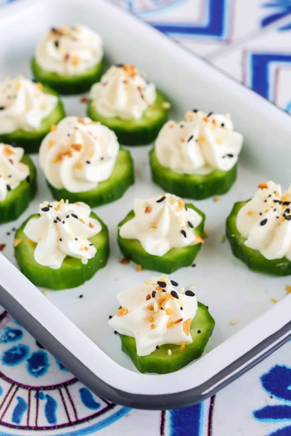 close-up view of sliced mini cucumbers, with piped cream cheese on top, sprinkled with everything bagel seasoning.