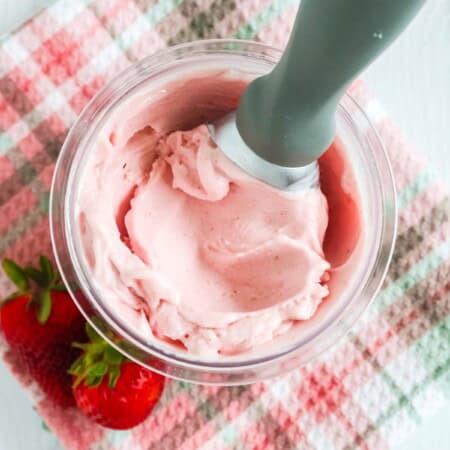 Ninja Creami strawberry gelato in a pint container, with an ice cream scoop in it, and two fresh strawberries next to it.