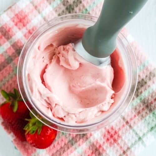 Ninja Creami strawberry gelato in a pint container, with an ice cream scoop in it, and two fresh strawberries next to it.