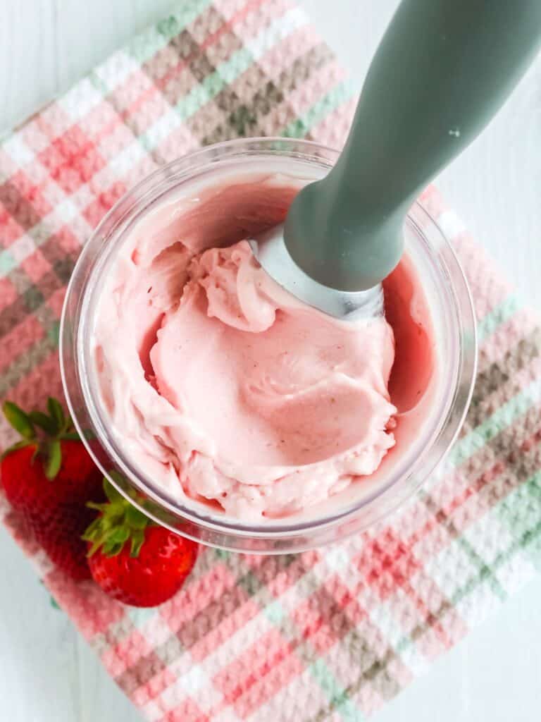 Ninja Creami strawberry gelato in a pint container, with an ice cream scoop in it, and two fresh strawberries next to it.