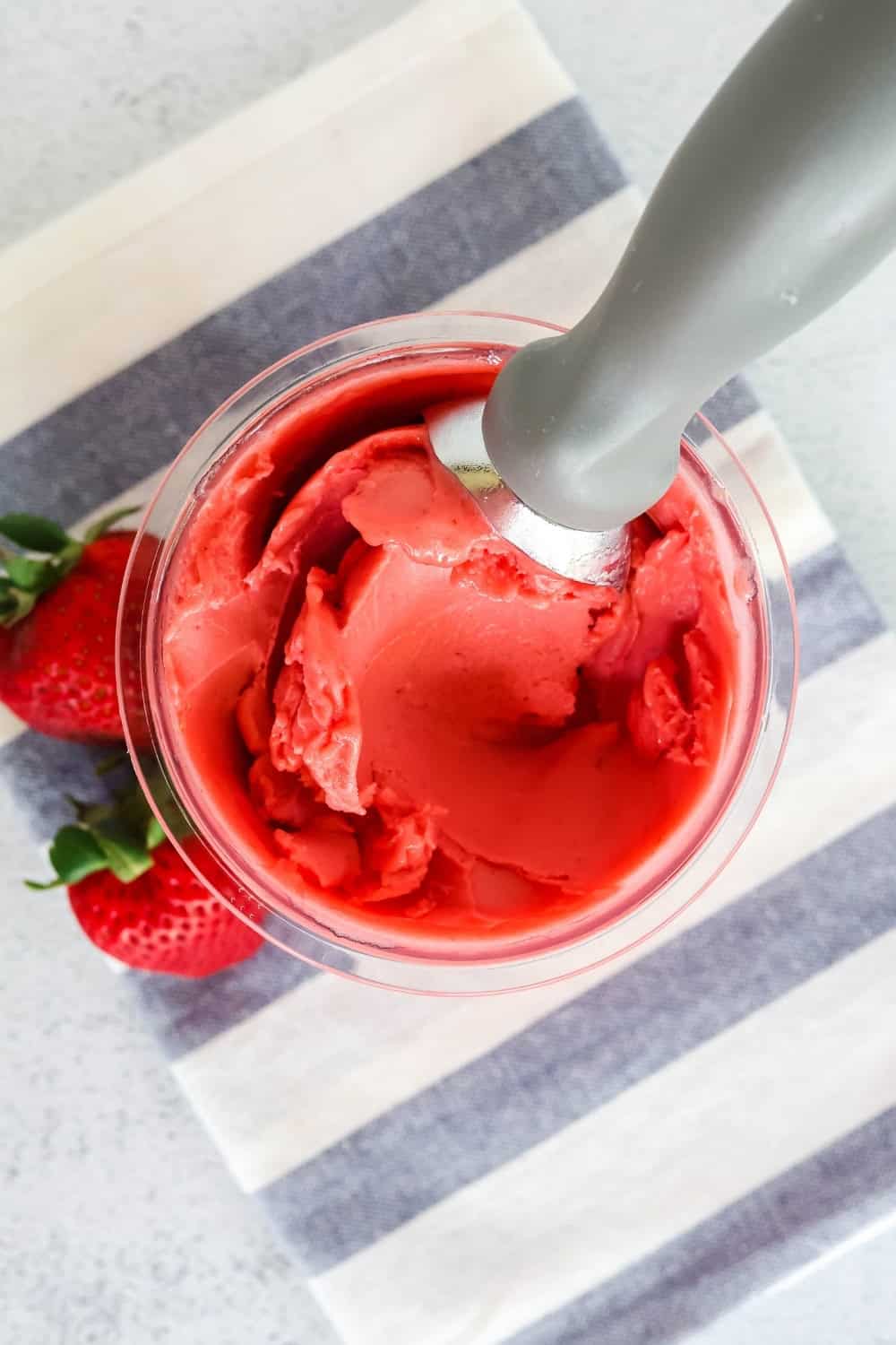 overhead view of a pint of strawberry sorbet made in the Ninja Creami. Two fresh strawberries are next to the pint container.