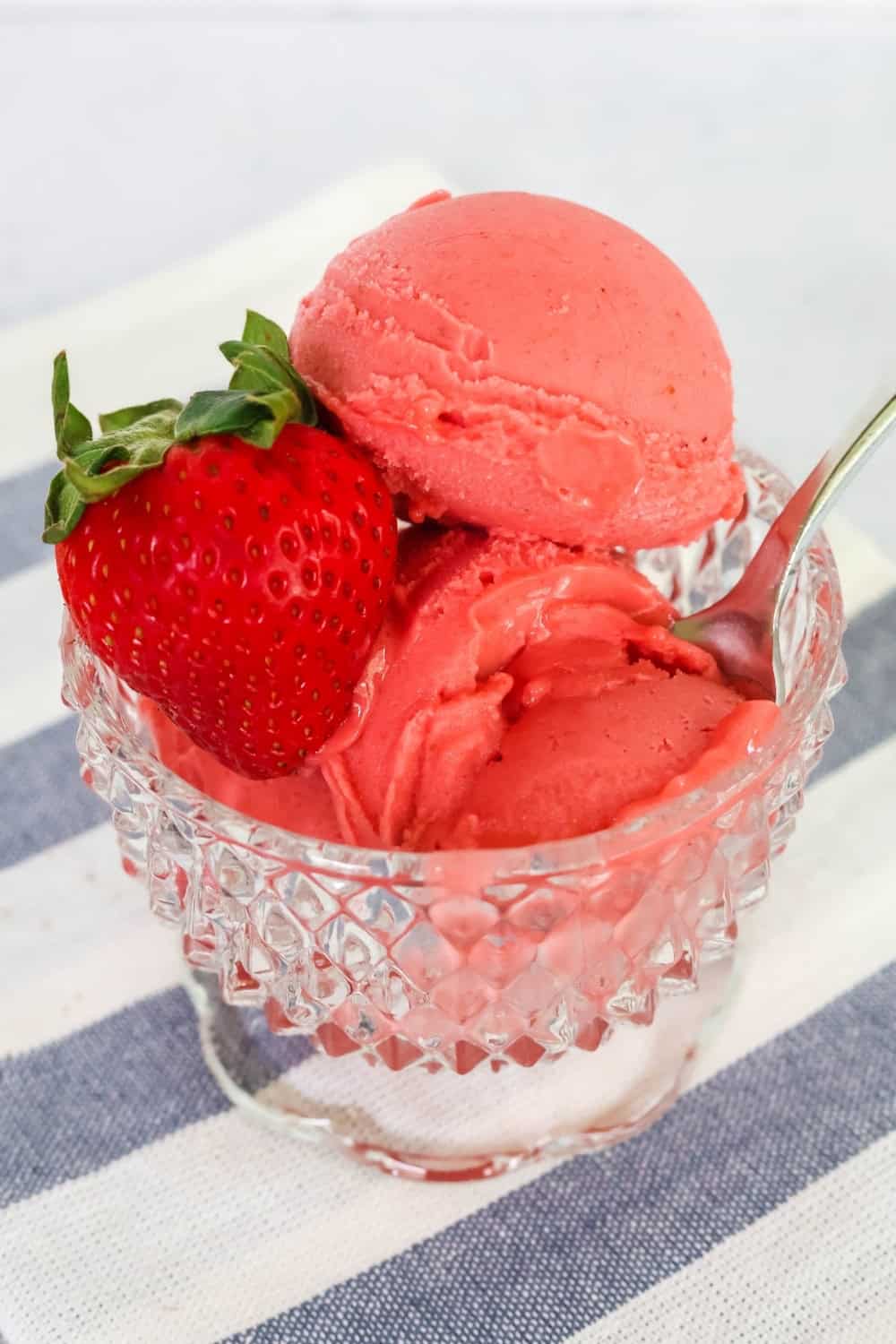 close-up view of scoops of fresh strawberry sorbet served in a glass dessert cup, garnished with a fresh strawberry.