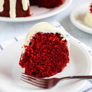 slice of red velvet pound cake, made from a mix, topped with cream cheese icing, served on a white plate.