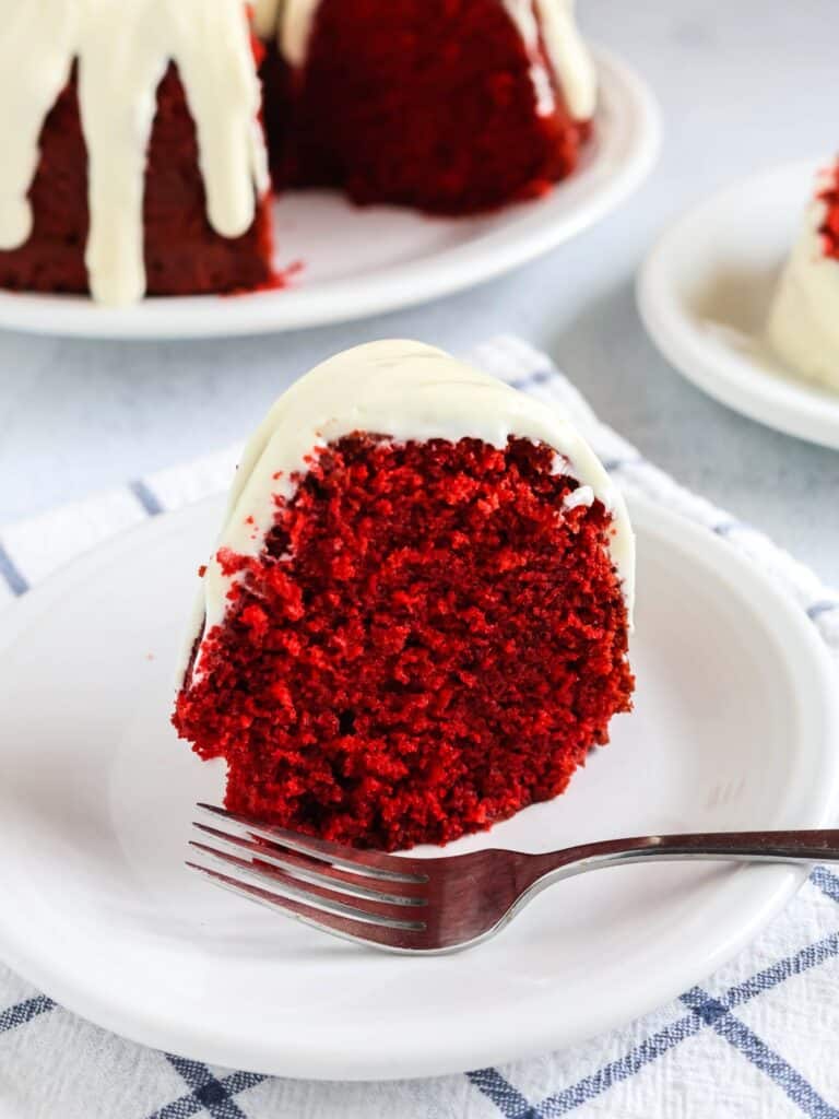 slice of red velvet pound cake, made from a mix, topped with cream cheese icing, served on a white plate.