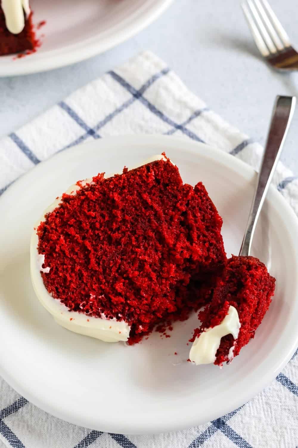 a fork cuts a bite out of a slice of cake mix red velvet pound cake, which is served on a white plate.