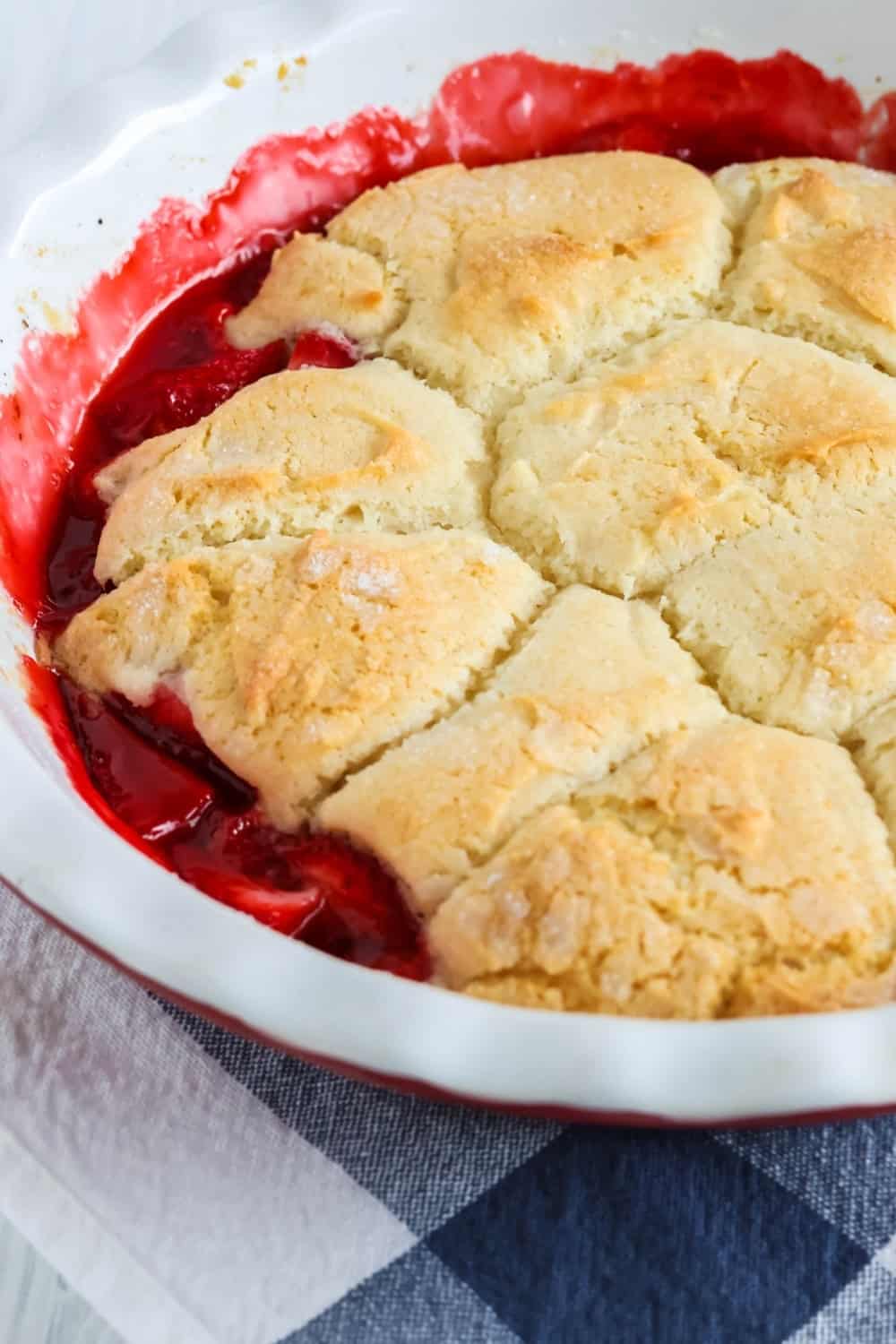 close-up side view of freshly baked strawberry cobbler in a deep dish pie pan, showing the ruby red filling and the golden-brown biscuit-like topping.