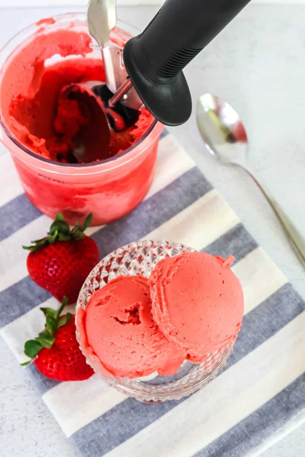 overhead view of a Ninja Creami pint of easy strawberry sorbet, along with a dessert cup containing scoops of the sorbet.