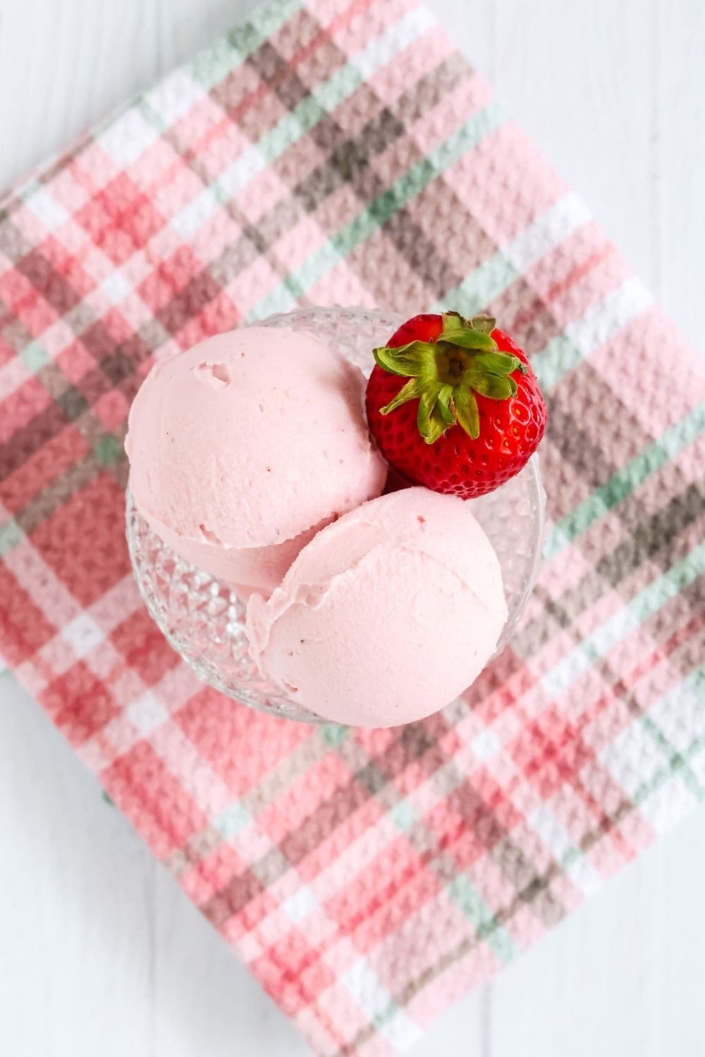 overhead view of scoops of homemade, eggless strawberry gelato in a glass dish, garnished with a fresh strawberry.