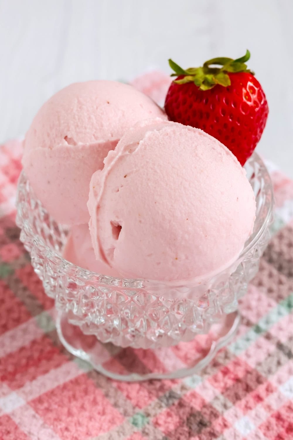 close-up view of scoops of strawberry gelato served in a glass dessert cup, garnished with a fresh strawberry.