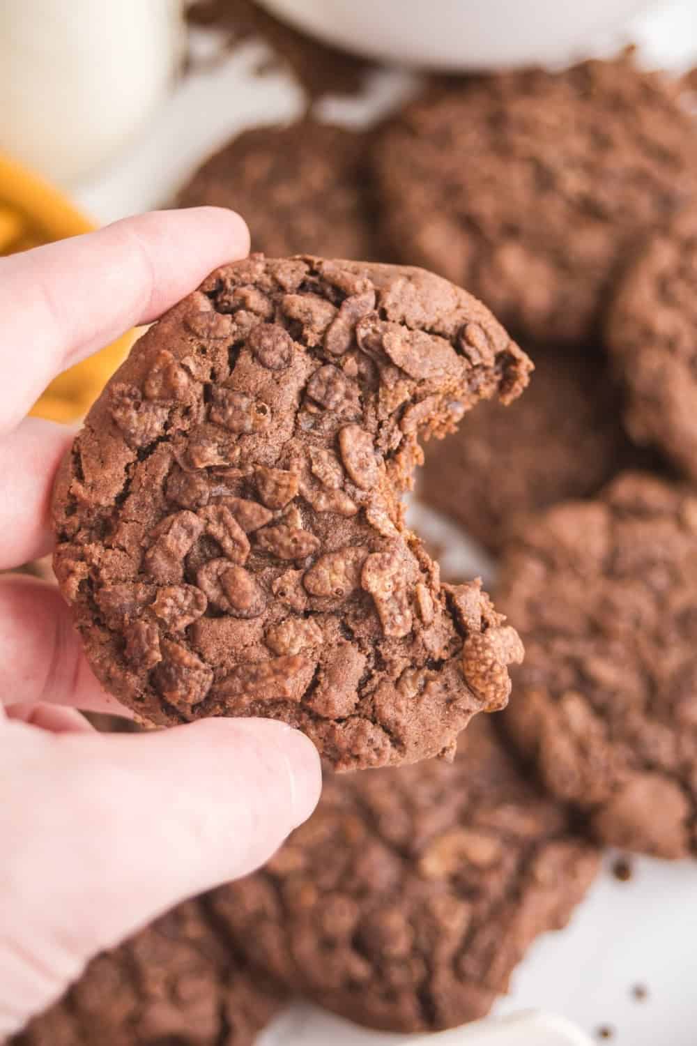 a hand holds a Cocoa Pebbles cookie that has a bite taken out of it.