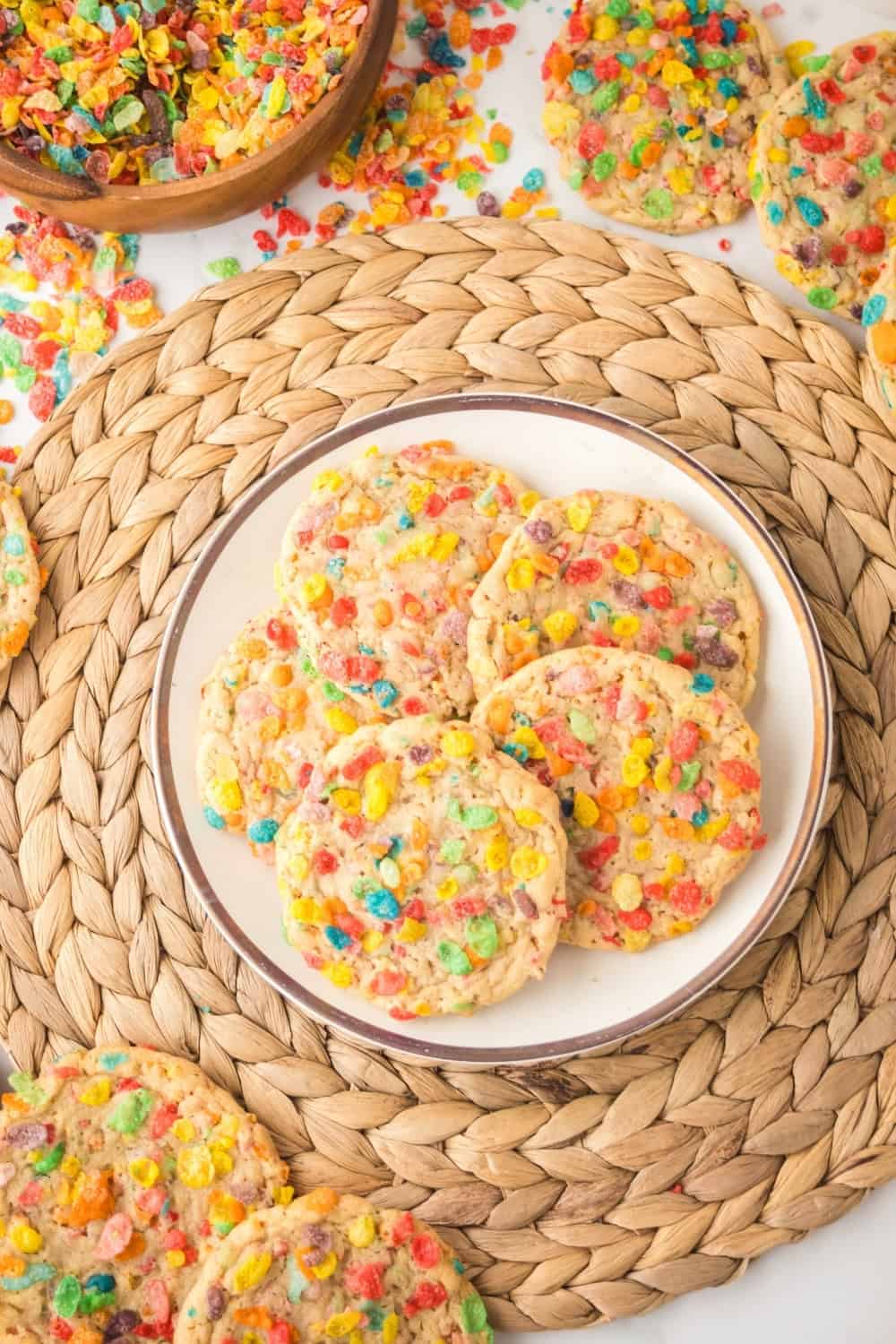 overhead view of a plate of soft and chewy Fruity Pebbles cookies on a straw placemat.
