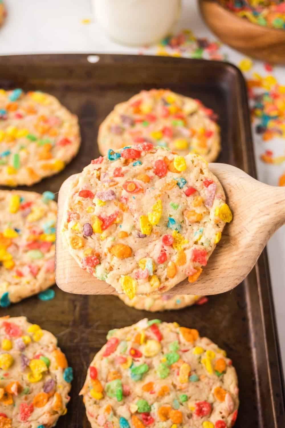 a spatula lifts a cookie made with Fruity Pebbles off of the baking sheet.