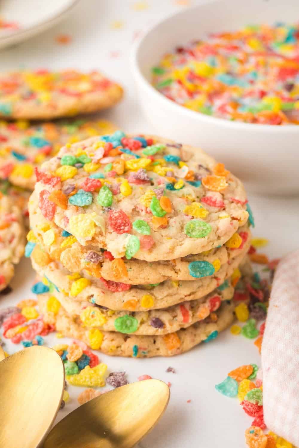 a stack of colorful Fruity Pebbles cookies in front of a white bowl of cereal.