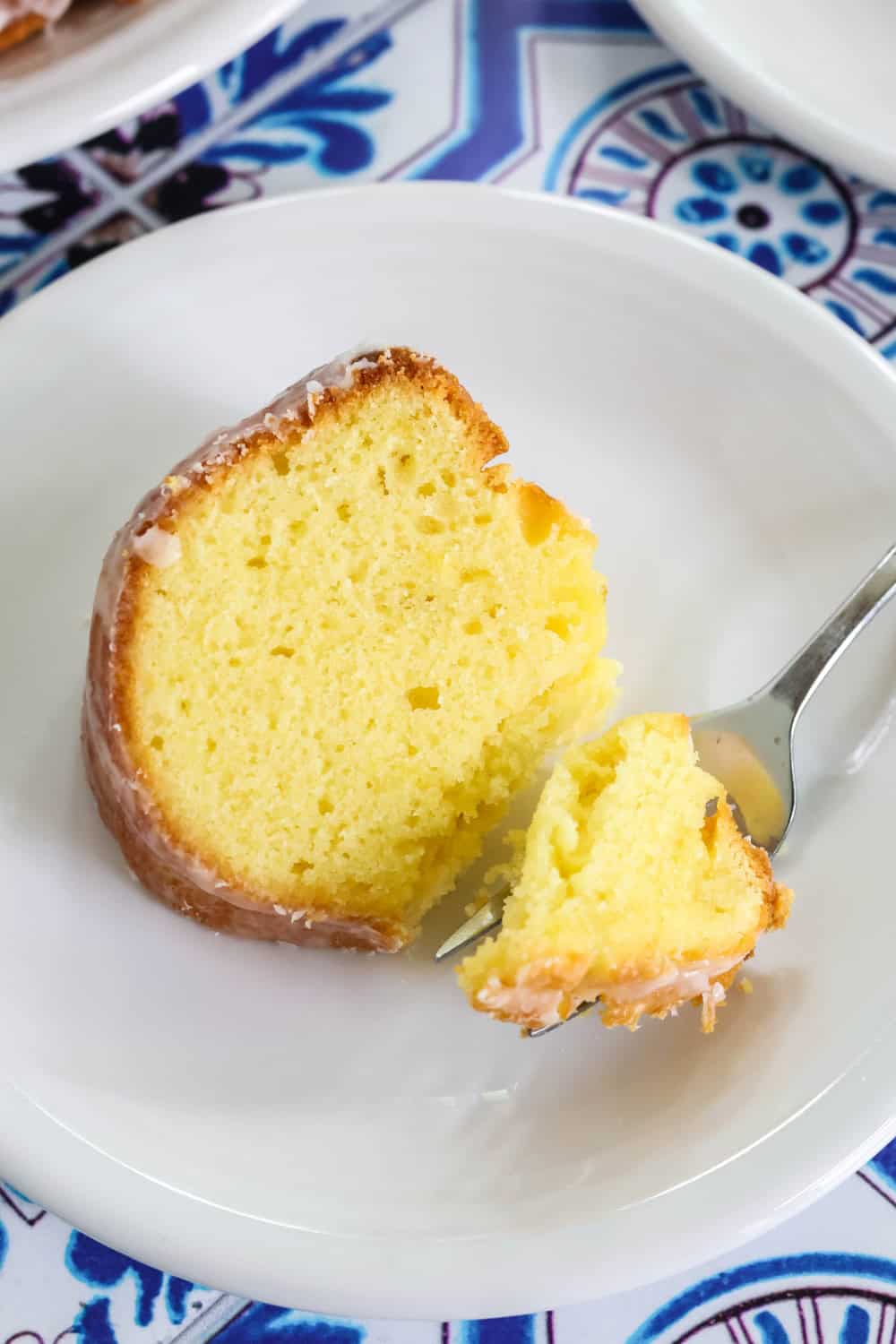 close-up view of a slice of lemon bundt cake made with mayonnaise. A fork has cut a bite out of the cake, showing the moist and tender texture. The cake is topped with a satiny lemon glaze.