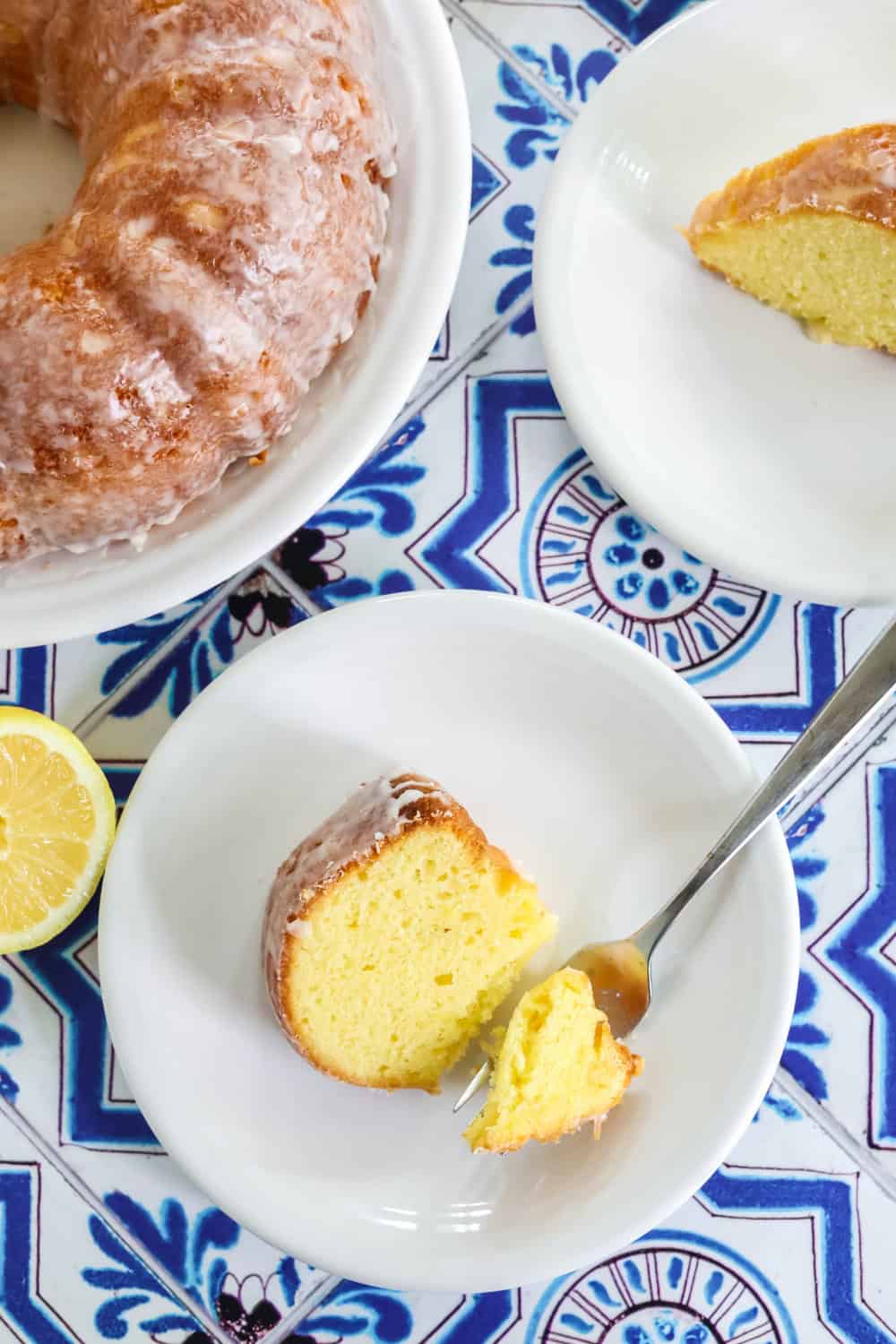 overhead view of a white plate serving a slice of lemon cake made with mayonnaise, and a fork has cut a bite out of the cake.