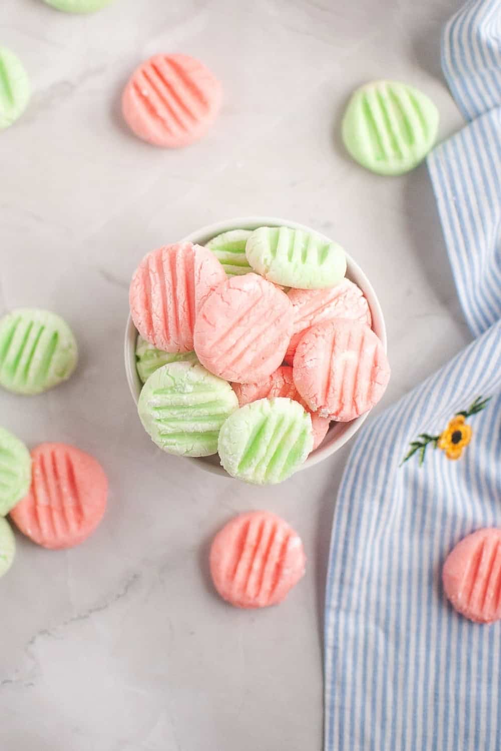 overhead view of homemade sugar-free cream cheese mints served in a white bowl, with more scattered around the bowl.