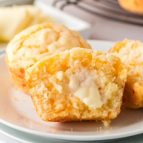 close-up view of two Bisquick cheesy muffins on a white plate. One of the muffins has been cut in half, with butter spread on the soft interior of the muffin.