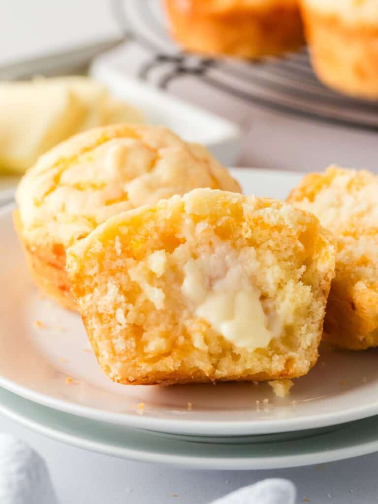 close-up view of two Bisquick cheesy muffins on a white plate. One of the muffins has been cut in half, with butter spread on the soft interior of the muffin.