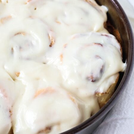 Bisquick cinnamon rolls, topped with cream cheese icing, in a round cake pan.
