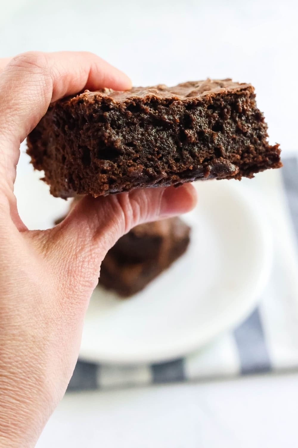 a woman's hand holds a brownie made with pudding mix and brownie mix.