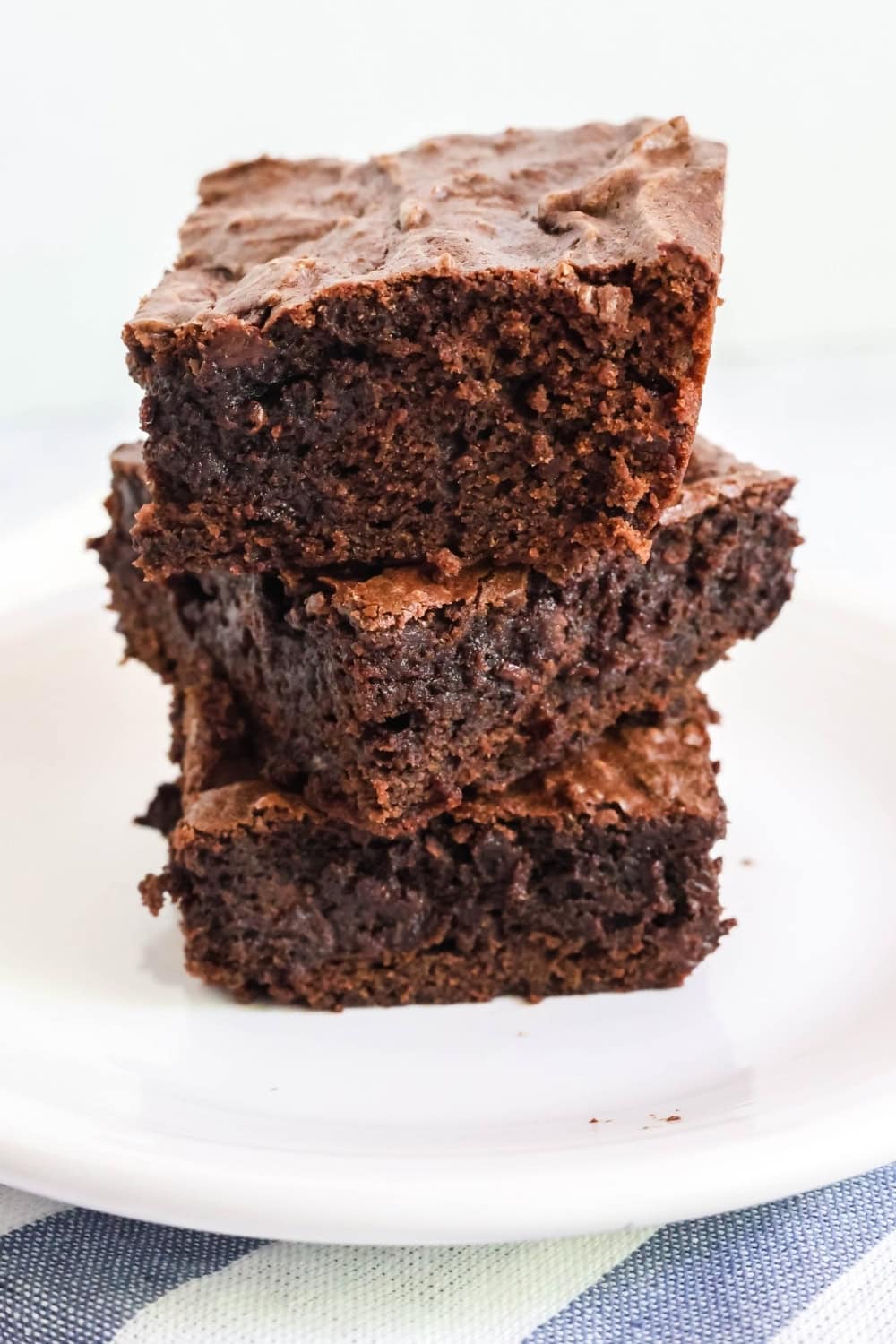 three double chocolate brownies stacked together on a white plate.