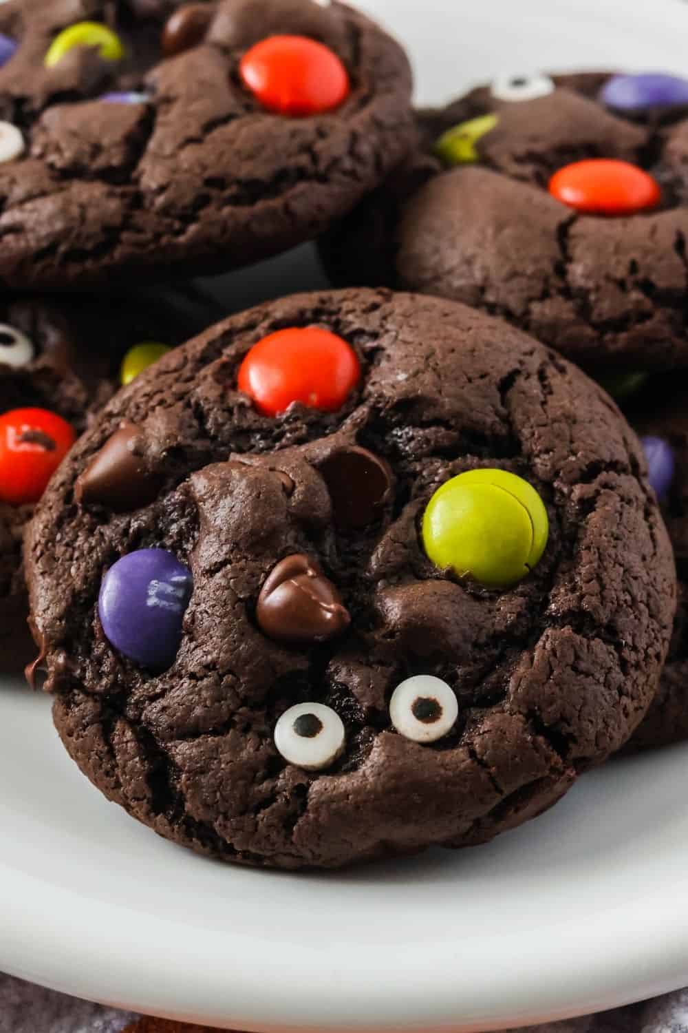 close-up of a chocolate cake mix cookie for Halloween, dotted with purple, orange, and green M&Ms and candy eyeballs.