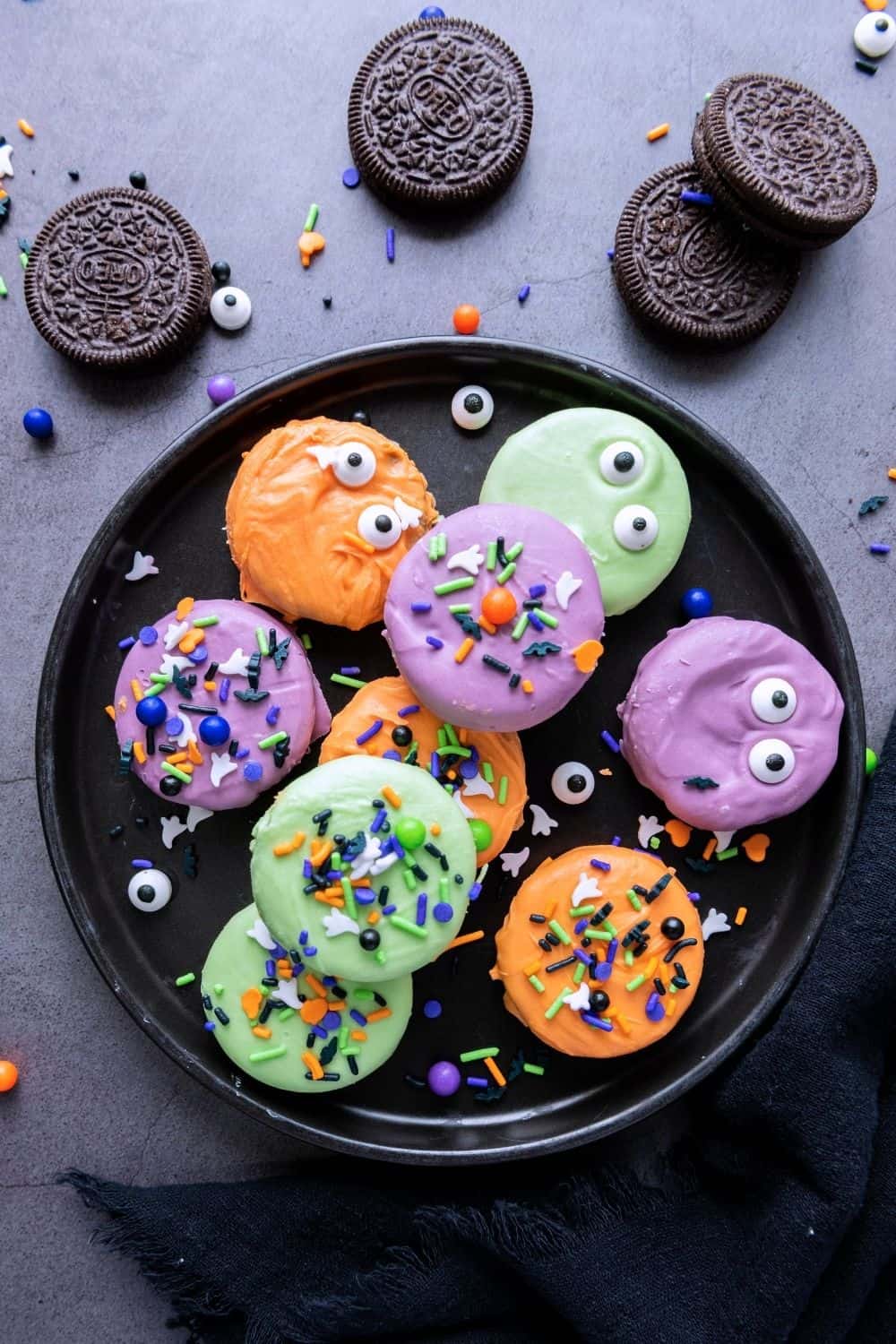 overhead view of a black plate with colorful Halloween dipped Oreos on it. Plain Oreos are scattered around the plate.